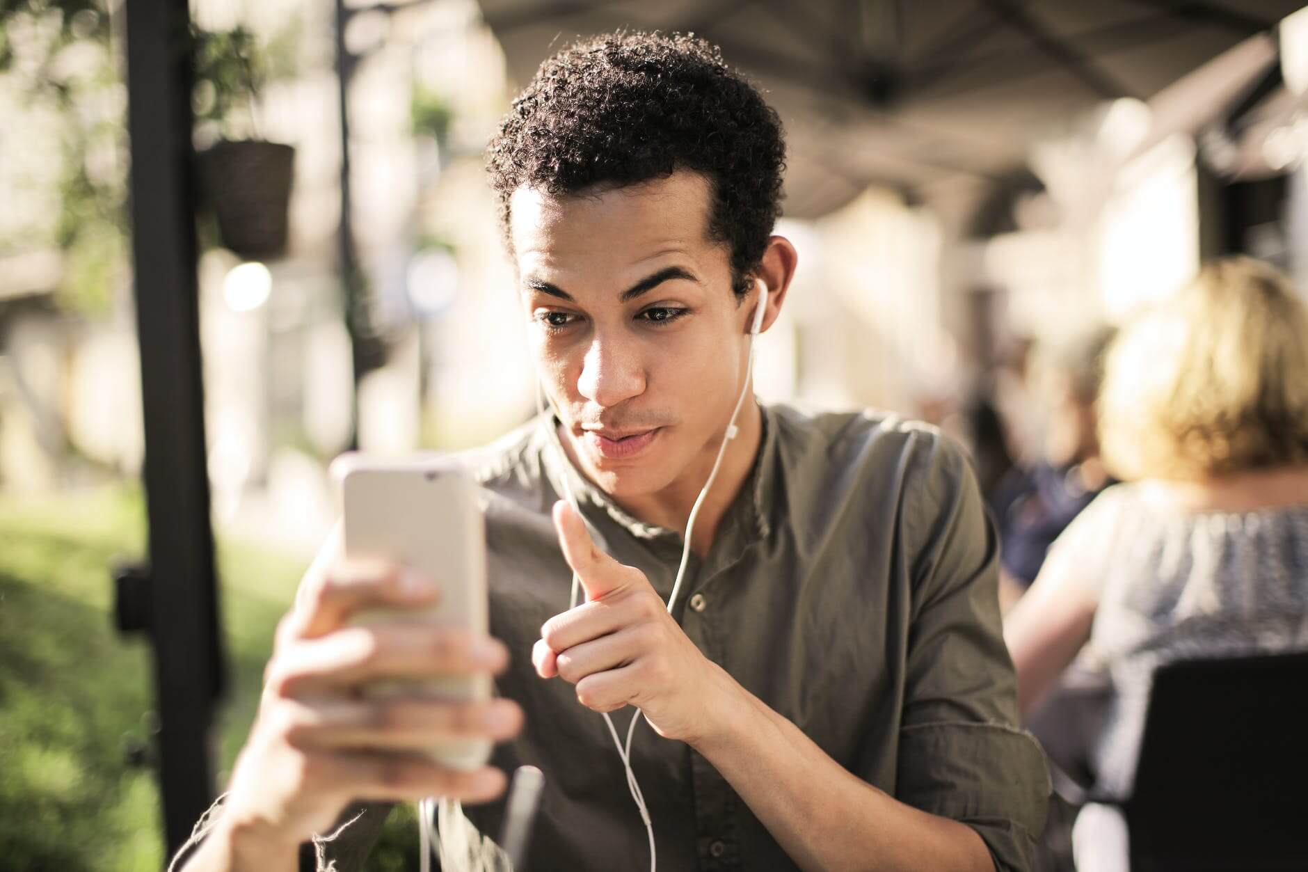Seorang pria mengenakan earphone sambil menatap layar ponsel